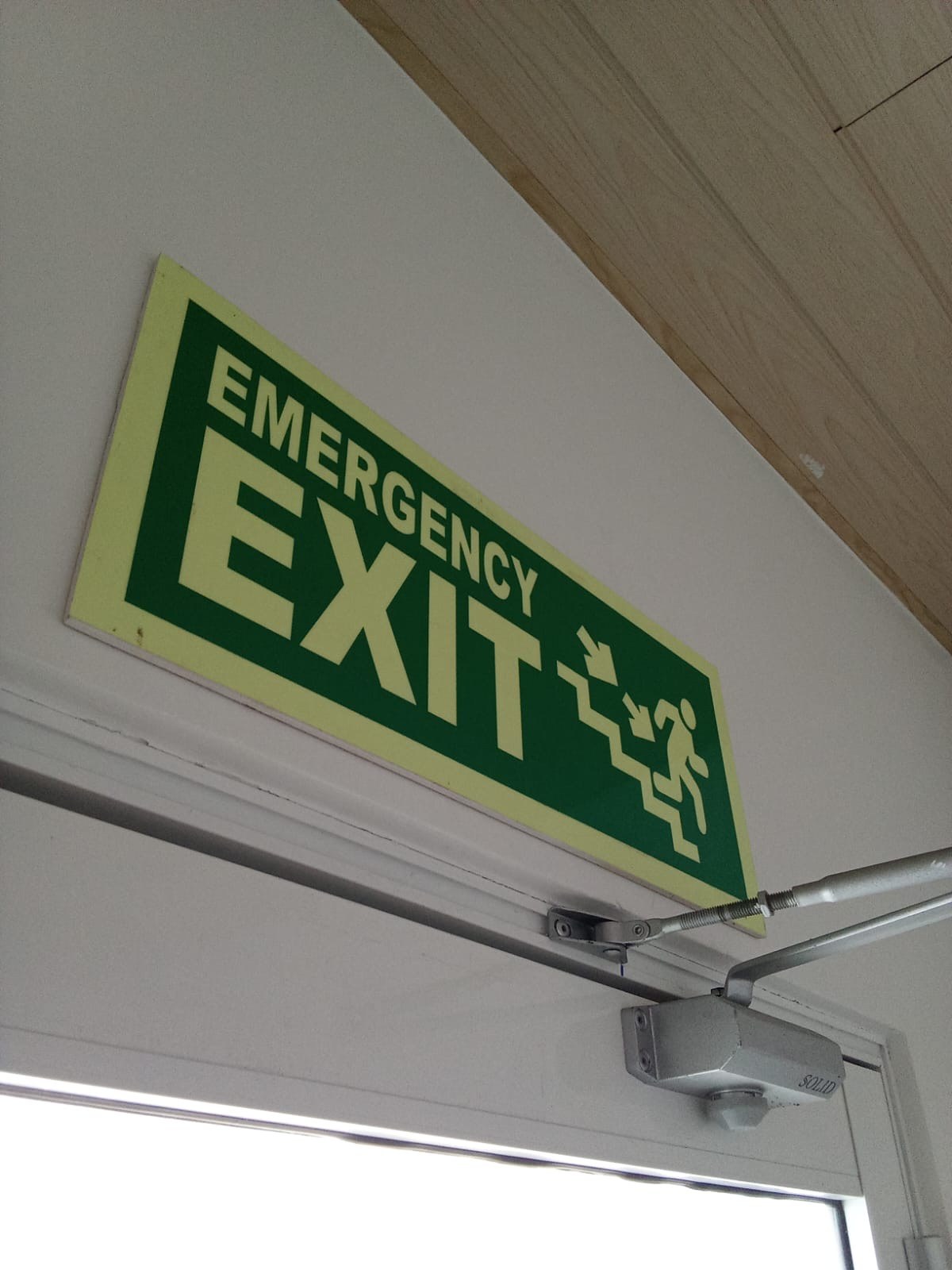 Overhead suspended emergency exit luminaire installed along central factory walkway