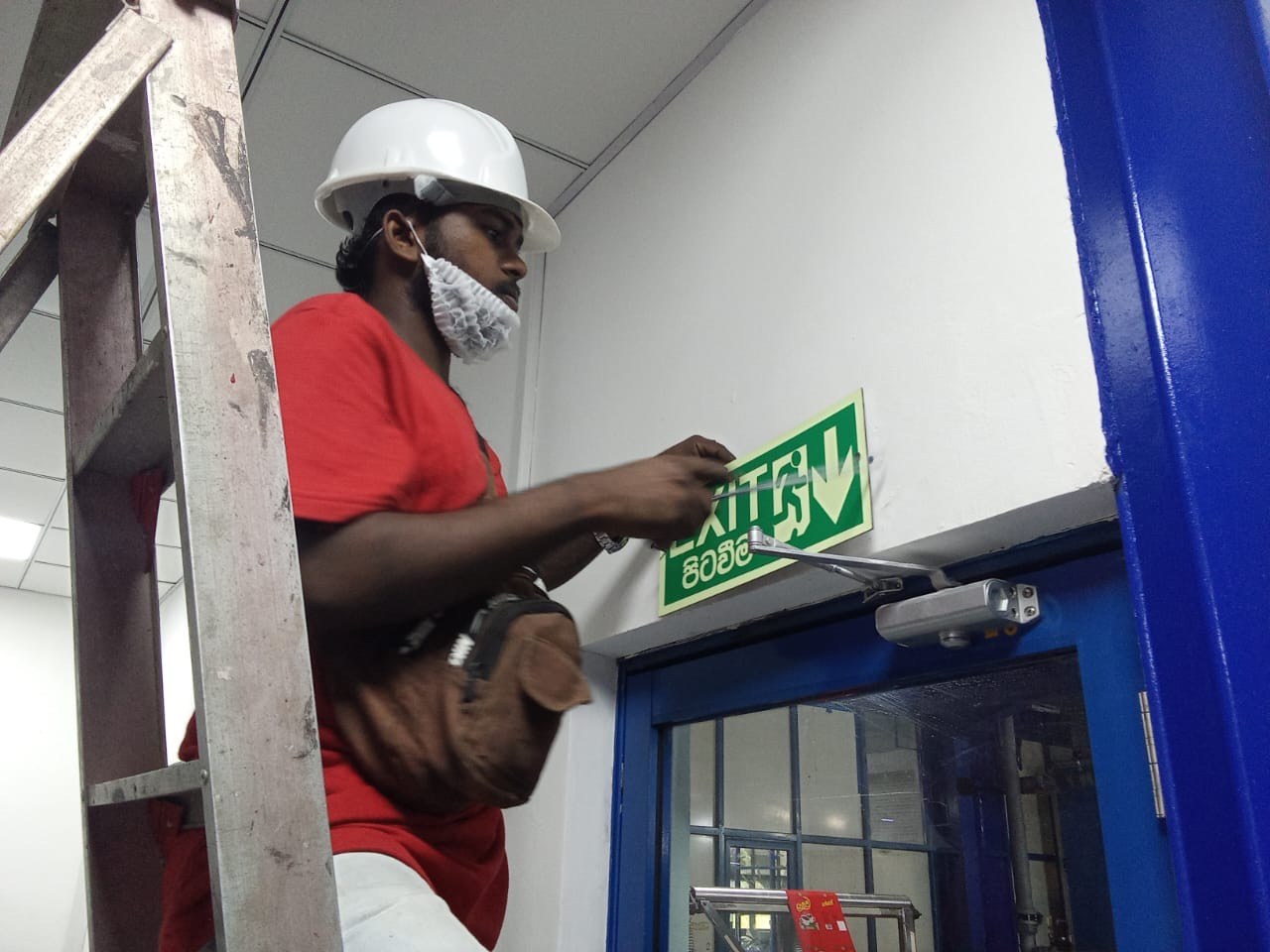 Certified technician calibrating illuminated exit sign above emergency escape door